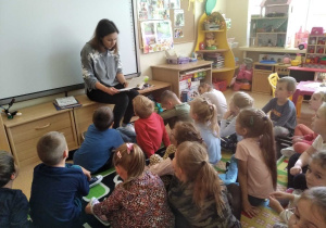 Dzieci z siedzą na dywanie a pani psycholog czyta im bajki