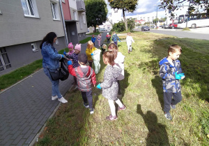 dzieci zbierają i segregują śmieci na skwerku przy bloku