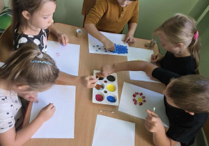Dzieci przy stolikach tworzą pacę urzywając patyczków kosmetycznych, rolek po papierze toaletowym, wacików i pomponów