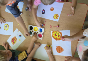 Dzieci przy stolikach malują farbami używając wacików kosmetycznych, pomponów, rolek po papierze toaletowym i wacików