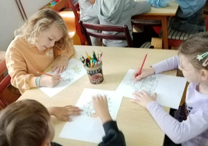 Dzieci kolorują przy stolikach rysunek dyni