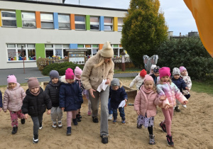 Grupa dzieci wraz z nauczycielką przelicza liczbę kroków od piaskownicy do zjeżdżalni.