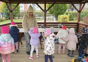 W altance nauczycielka trzyma torbę do której dzieci wkładają i przeliczają ukryte skarby.