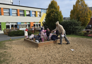 Dzieci w piaskownicy szukają ukrytych skarbów. Nauczycielka zbiera znalezione przez dzieci skarby.