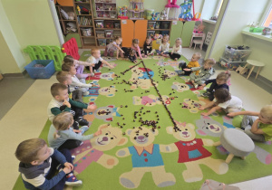 dzieci siedzą na dywanie i pokazują ułożoną na środku z kasztanów cyfrę jeden.