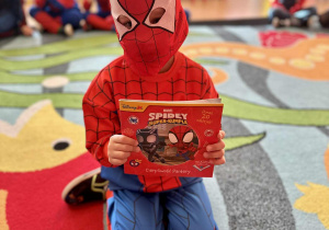 Chłopiec w kostiumie Spidermana z książeczką o tej tematyce
