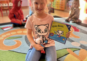Dziewczynka w bluzeczce Kici Koci, oraz z książeczką i pluszakiem z tej bajki