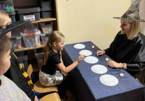 Dziewczynka wybiera jeden z 5 talerzyków, przedmiot ukryty pod nim określa, jakie życie czeka dziewczynkę