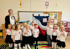 Dzieci z grupy Biedronek wraz z nauczycielką stoją przy patriotycznej tablicy