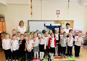 Dzieci z grupy Pszczółek wraz z nauczycielką stoją przy patriotycznej tablicy