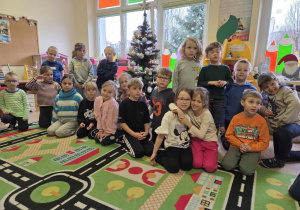 Dzieci siedzą i stoją przy ubranej choince