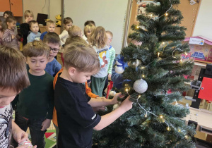 Dzieci zawieszają białe bombki na choince