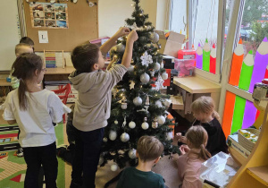 Dzieci dekorują choinkę ozdobami