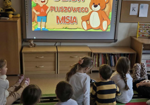 Dzieci oglądają na tablicy multimedialnej film edukacyjny o Święcie Pluszowego Misia