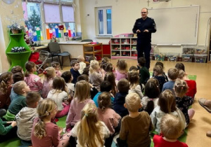 Policjant rozmawia z dziećmi na temat bezpieczeństwa na drodze i unikania kontaktu z obcymi osobami