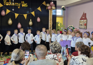 Dzieci ustawione w półkolu śpiewają piosenkę "Koncert dla babci i dziadka"