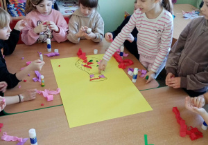 Dziewczynki i chłopcy tworzą wspólną pracę plastyczną z okazji ich święta