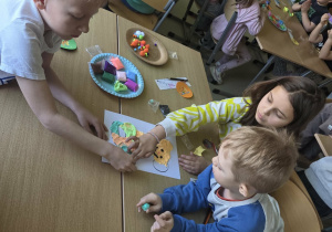 Dzieci w grupach wylepiają plasteliną postać Plastusia