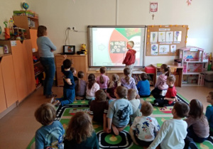Chłopiec rozwiązuje na tablicy multimedialnej zagadki dotyczące wiosennych kwiatów