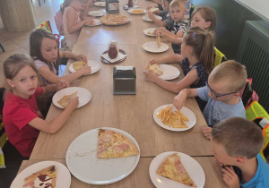 Dzieci jedzą pizzę przy stoliku