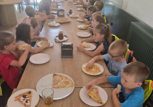 Dzieci jedzą pizzę przy stoliku