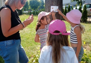 Dzieci wraz z wychowawczynią przyczepiają do drzewa kopertę z zadaniem do wykonania dla Misiów