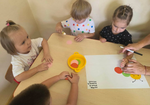Dzieci przyklejają kolorowe kółka tworząc grupową gąsienicę