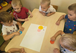 Dzieci kolejno przyklejają kolorowe kółka tworząc grupową gąsienicę