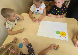 Dzieci przyklejają kolorowe kółka tworząc grupową gąsienicę