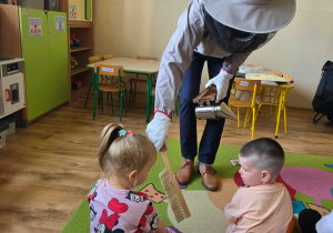 Pszczelarz prezentuje zestaw potrzebny w jego pracy: dłuto, miotełkę i podkurzacz