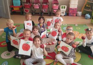 Dzieci pozują do zdjęcia z pracami plastycznymi przedstawiającymi jabłka