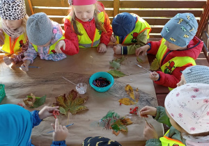 Dzieci w altanie przyklejają jarzębinę i liście na karton