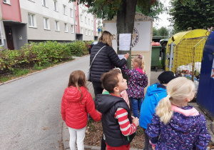 Dzieci wraz z nauczycielką przyklejają kopertę z zadaniem do drzewa