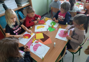 Dzieci wyklejają kolorowymi papierami rysunek konturowy jabłka