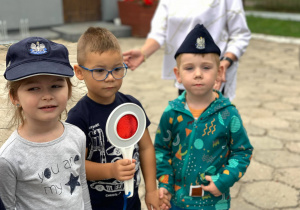 Dzieci w czapce policyjnej i z "lizakiem" pozują do zdjęcia