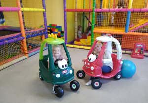 Dwie dziewczynki jeżdżą autkami po sali zabaw