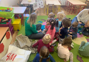Dzieci słuchają czytanej przez bibliotekarkę książki