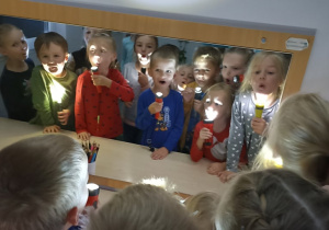 Aneta Szymańska Gra w podchody. Dzieci stoją w sali logopedycznej przed lustrem świecąc latarkami na twarz.