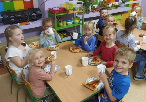 Dzieci jedzą kolację: pizzę i piją herbatę przy stoliku.