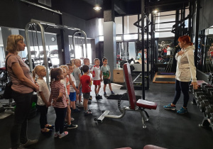 Pani Kamila oprowadza dzieci i nauczycielkę po siłowni