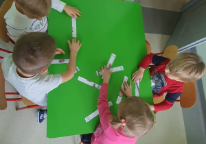 Praca w grupach dzieci przy stoliczku układają bajkowe puzzle