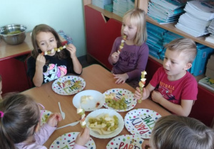 Dzieci jedzą zrobione przez siebie szaszłyki owocowe