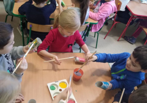 Dzieci przy stolikach malują rolki po papierze toaletowym (kredka)