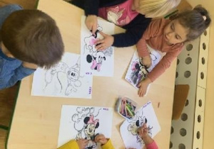 Dzieci przy stolikach kolorują Myszkę Miki i Myszkę Minnie