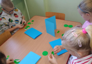 Dzieci zginają na pół papierowe koła koloru zielonego tworząc choinkę