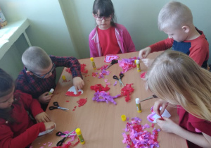 Dzieci przyklejają kawałki bibuły na papierowe serce