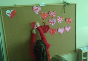 Dzieci kolejno przytwierdzają swoją walentynkę na korkowej tablicy