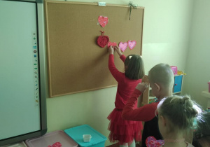 Dzieci przytwierdzają swoją walentynkę na korkowej tablicy