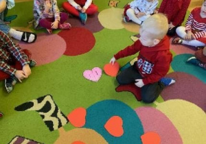 Dzieci przeliczają papierowe serca na dywanie