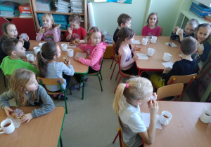 Dzieci z wielkim apetytem jedzą przy stoliku pączki
